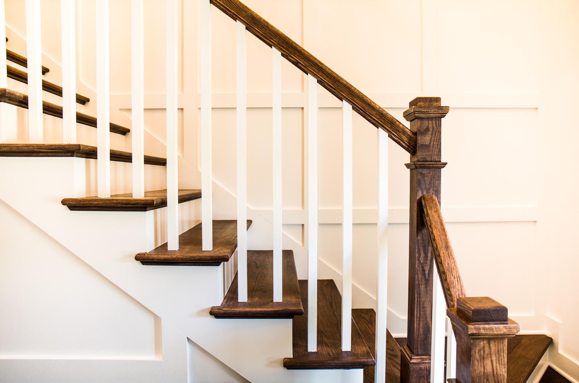 Dark natural wood staircase. White paneled walls.